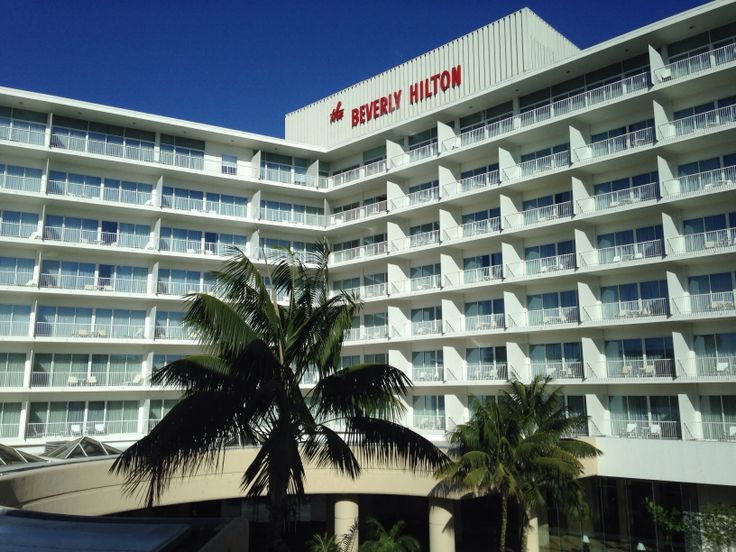 a hotel with palm trees in front of it and a large white building behind it