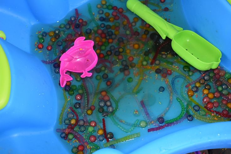 there is a toy frog in the bathtub filled with beads and other things to play with