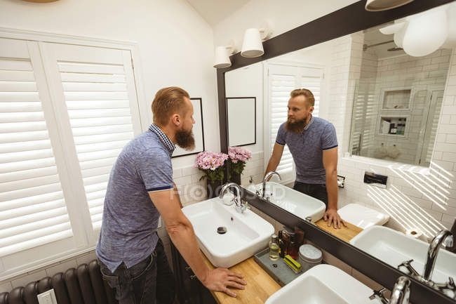 two men standing in front of a bathroom mirror looking at each other's reflection