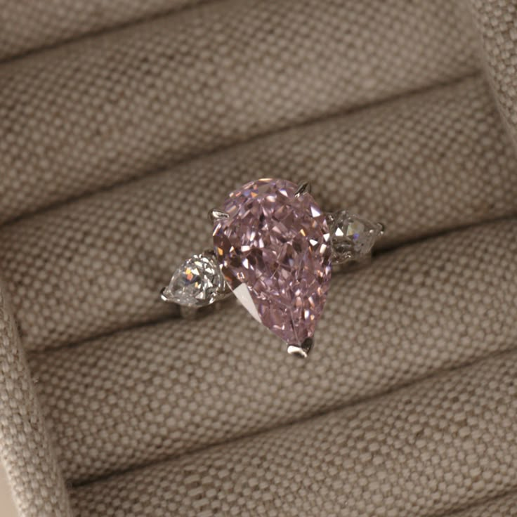 a pink diamond ring sitting on top of a cushion