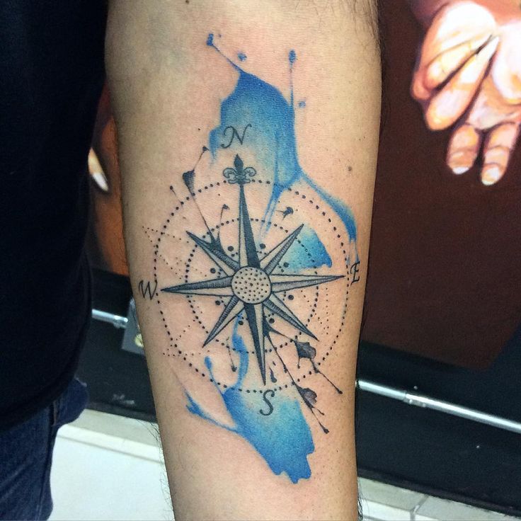 a man's arm with a watercolor compass tattoo on the left side of his arm