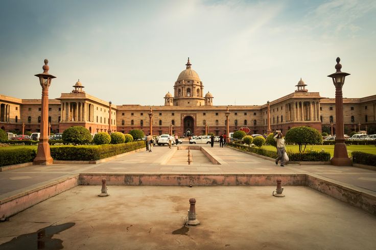 a large building with many pillars in front of it and people walking around the courtyard