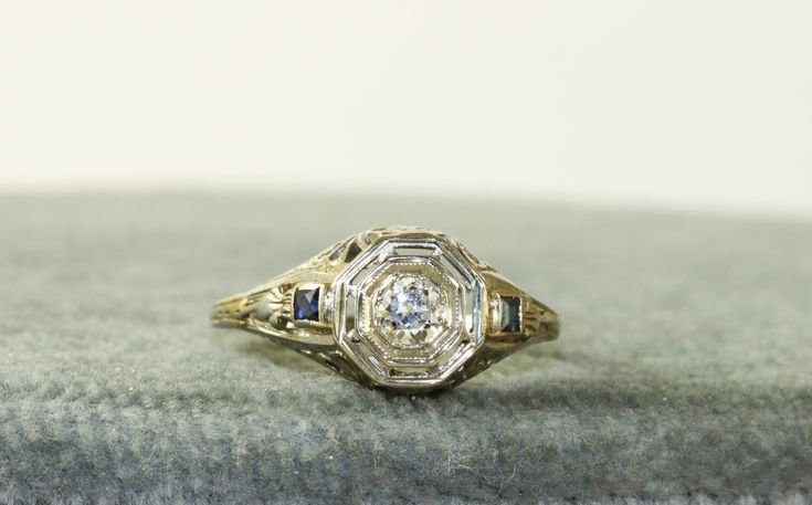 These early filigree rings are so pretty.  This is a Edwardian filigree band in 14KW gold with a 0.23CT Diamond and  side synthetic Sapphires.  Synthetic colored stones were common in the Edwardian era. This ring weighs 2.8 grams in size 5.5 and could be sized by your local jeweler. Anniversary Sapphire Ring With Filigree Fine Jewelry Style, Anniversary Fine Jewelry Sapphire Ring With Filigree, Fine Jewelry Sapphire Ring With Filigree Design, Vintage White Gold Sapphire Ring With Accent Stones, Art Deco Filigree Ring With Accent Stones For Anniversary, Antique Diamond Rings With Accent Stones, Fine Jewelry Filigree Ring With Accent Stones For Anniversary, Elegant White Gold Filigree Ring With Accent Stones, Classic White Gold Filigree Ring With Accent Stones