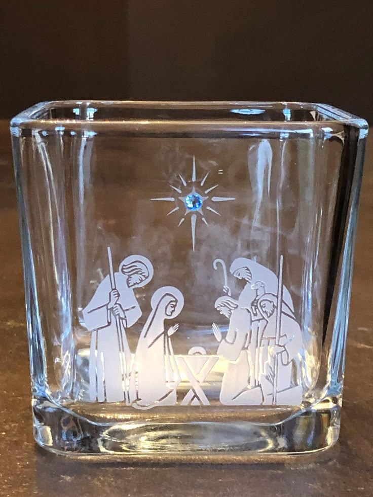 a glass with a nativity scene etched on the front and sides, sitting on a table