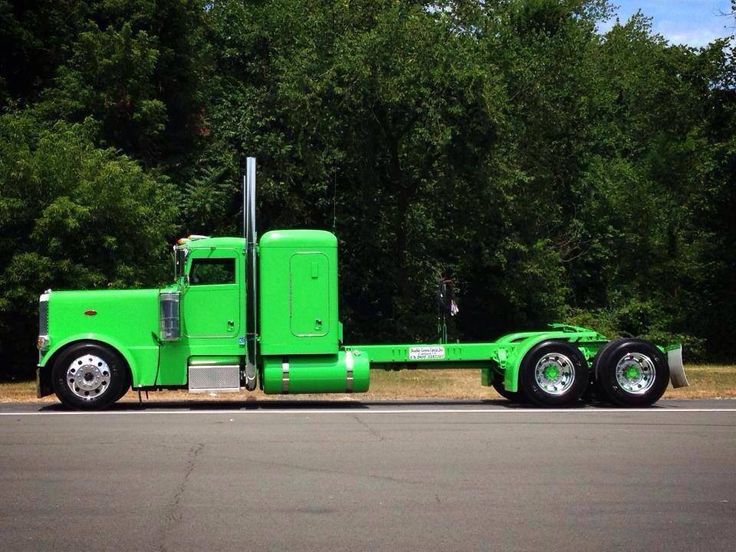 a bright green semi truck is parked on the side of the road in front of some trees