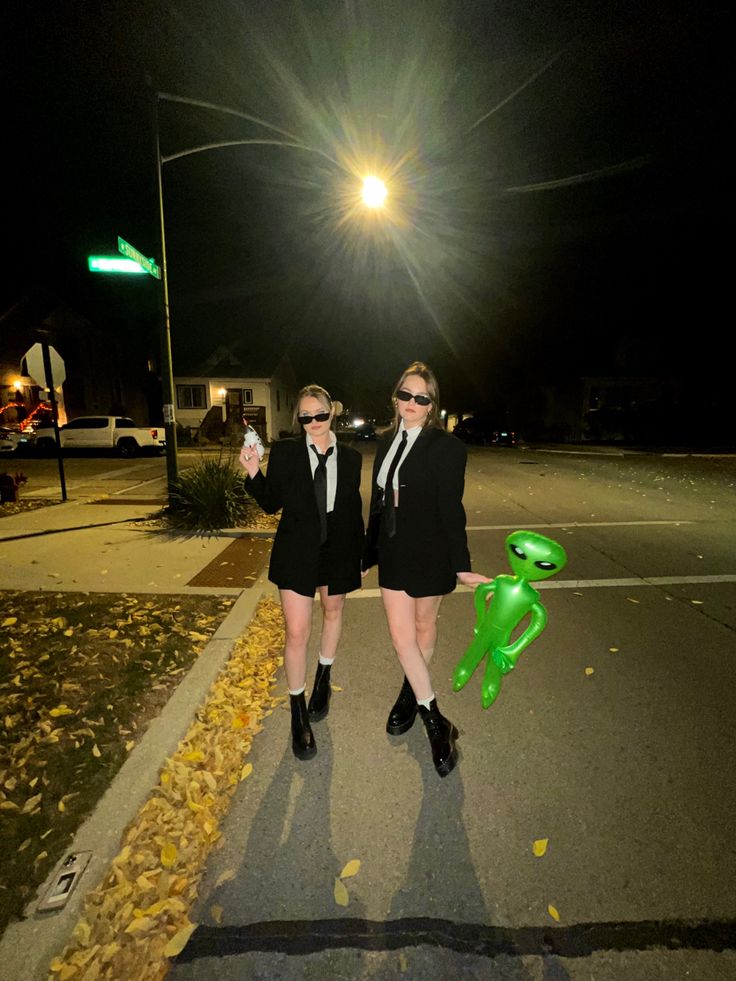 two women dressed in black and white posing for the camera on a street at night