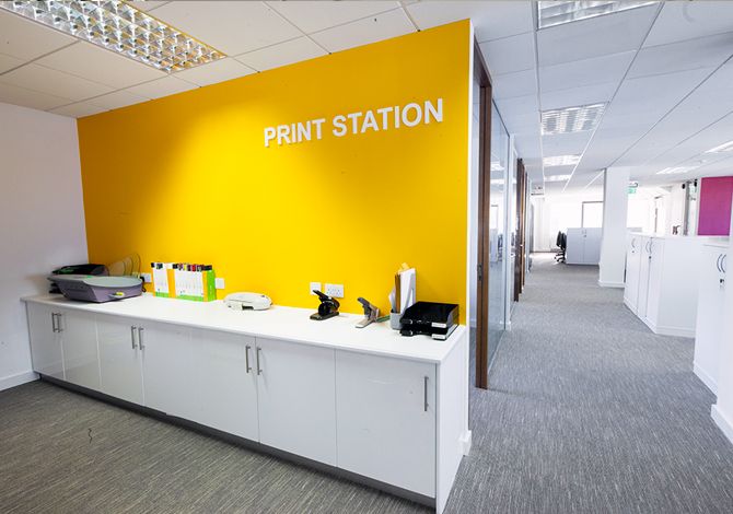 an office cubicle with yellow walls and printer station on the side wall, along with white cabinets