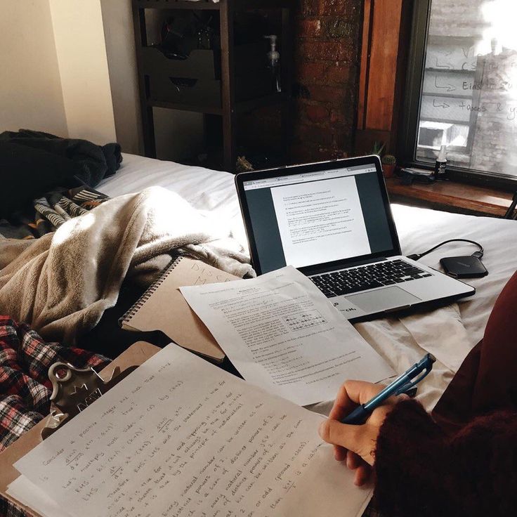 a person sitting in front of a laptop computer on top of a bed next to papers