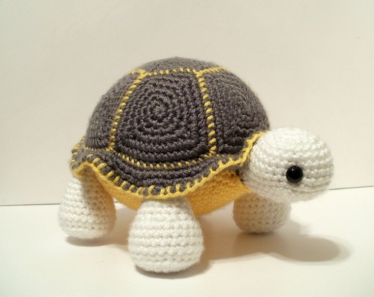 a small crocheted turtle is shown on a white surface with yellow and gray accents