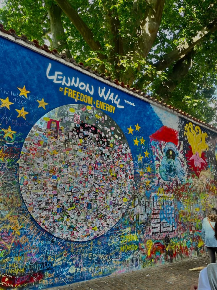 people walking past a wall covered in many different types of stickers and graffiti on it