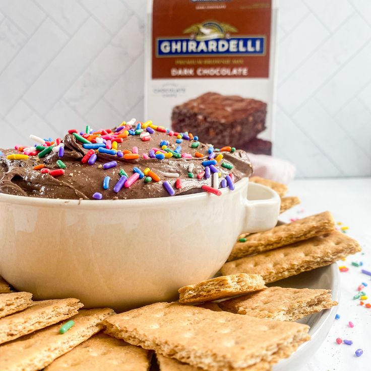 a bowl filled with chocolate frosting surrounded by crackers and sprinkles