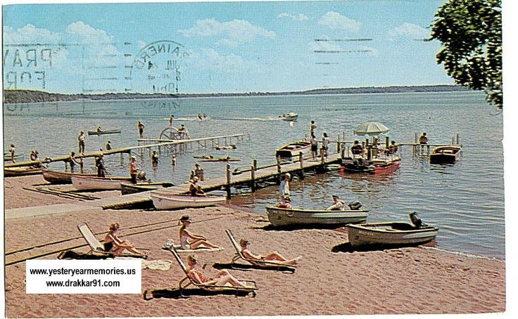 an old postcard shows people relaxing on the beach and in the water, with boats