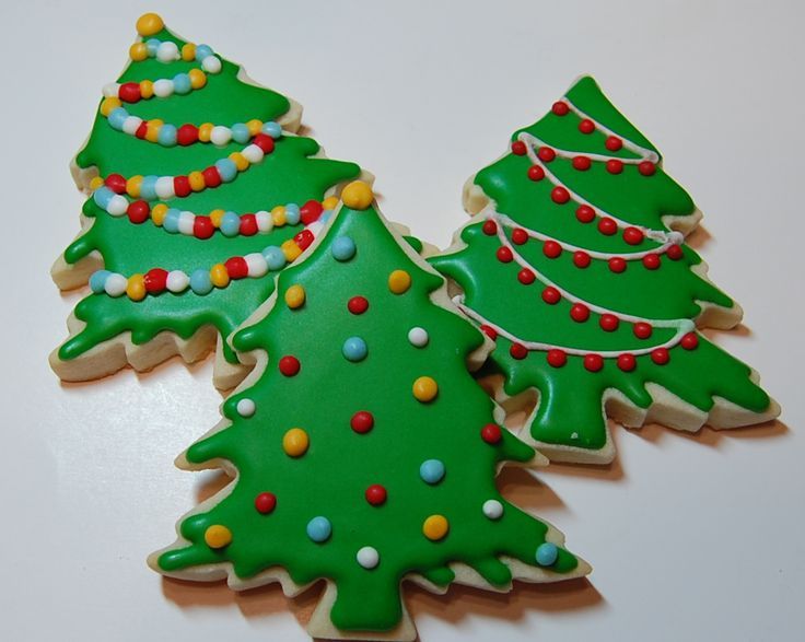 two decorated christmas tree cookies sitting on top of a table