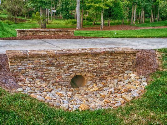 a stone wall with a hole in the middle surrounded by green grass and trees on either side