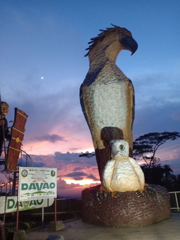 two stuffed animals sitting on top of a bird statue in front of a ...