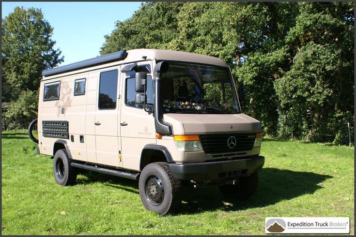 an off - road vehicle is parked on the grass in front of some trees and bushes