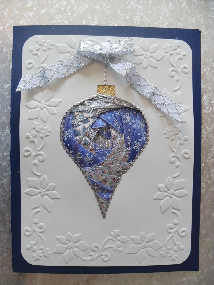 an ornament hanging from a ribbon on top of a white card with blue trim