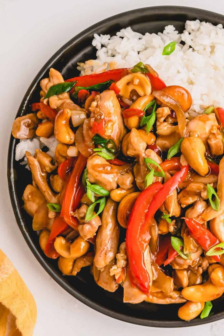 a black plate topped with cashews and red bell peppers next to white rice