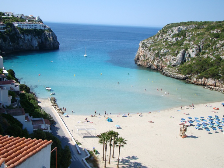 people are on the beach and in the water near an island with many trees, umbrellas and boats