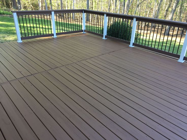 a wooden deck with white railings in the middle and trees in the back ground