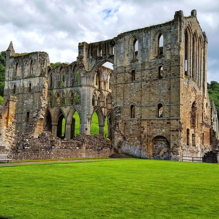 the ruins of an old castle with grass in front and trees in the back ground