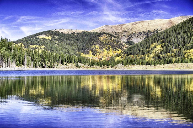 the mountains are reflected in the still water on the lake's surface, with pine trees lining the shore