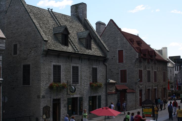 people are walking down the street in front of old stone buildings with red umbrellas