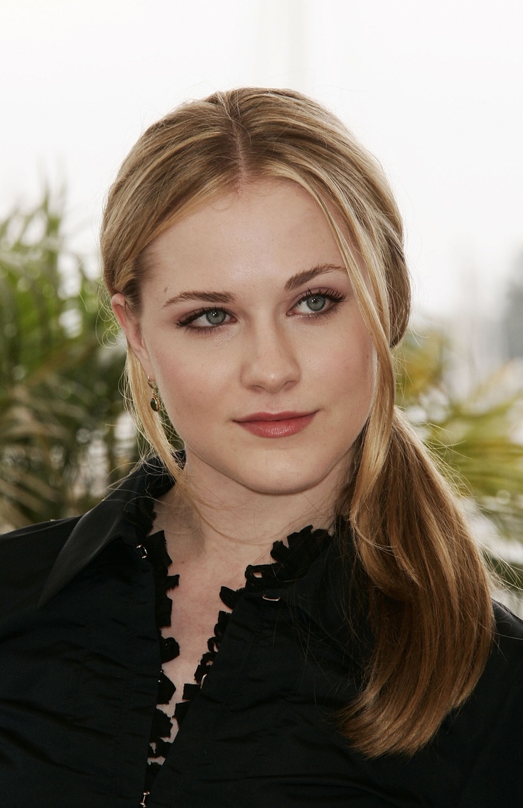 a woman with blonde hair and blue eyes posing for a photo in front of some plants