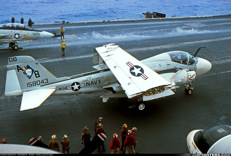 an airplane is parked on the flight deck of an aircraft carrier while several people watch