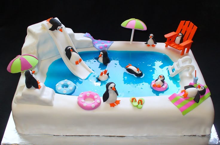 a birthday cake decorated with penguins and inflatable pool