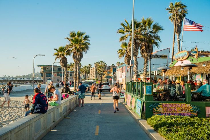 people are walking on the boardwalk near the beach and palm trees in front of them