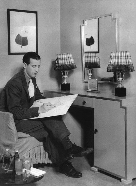 a man sitting at a desk in front of a mirror reading a book and holding a pen