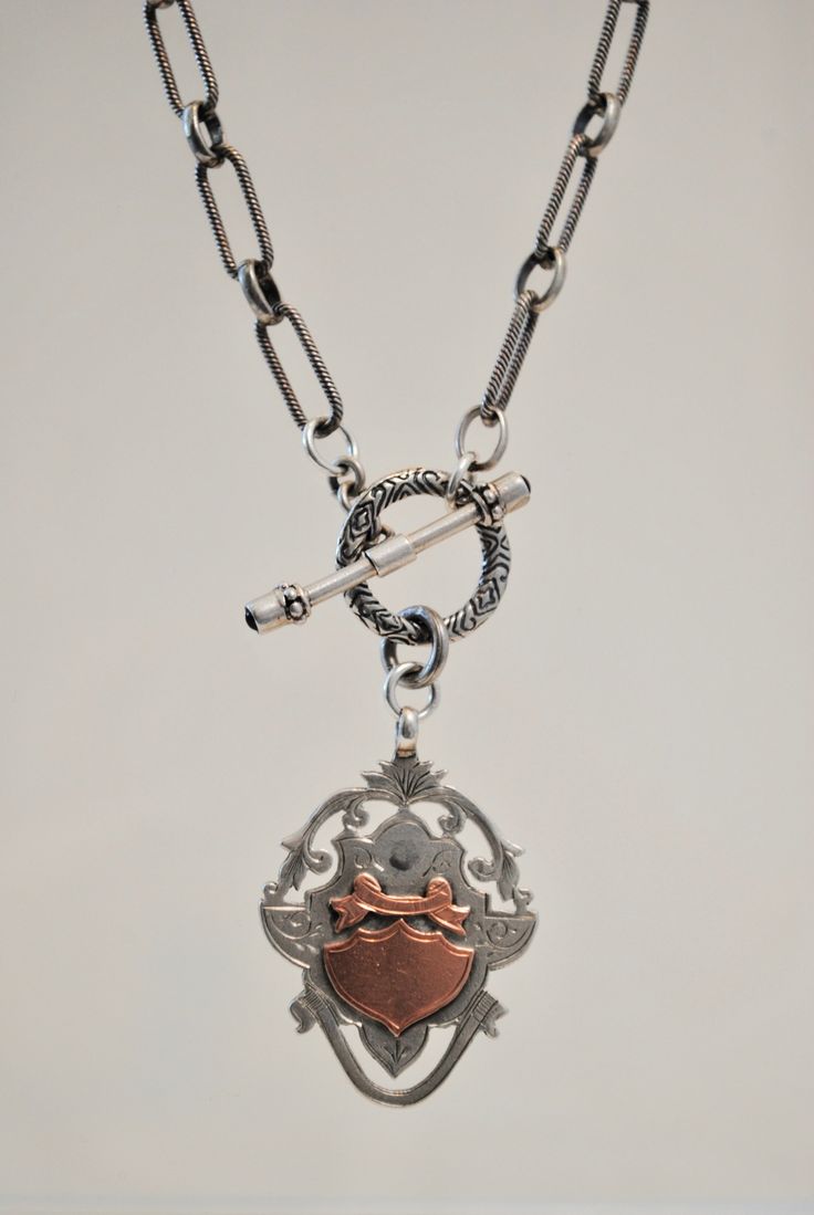 This exquisite Antique English Watch Fob Necklace is a carefully crafted heirloom piece, combining the elegance of sterling silver and the timeless beauty of 9k rose gold. This necklace is attached with a toggle, featuring two garnets. With an English seal embossed on the back of the pendant, this one-of-a-kind necklace is sure to be treasured for generations. Length: 18"Pendant: 1 1/2" Rose Gold Sterling Silver Medallion Jewelry, Classic Sterling Silver Toggle Necklace With Lobster Clasp, Timeless Silver Locket Jewelry, Luxury White Gold Jewelry With Toggle Clasp, Classic Sterling Silver Toggle Necklace, Luxury Silver Locket Jewelry, Classic Rose Gold Medallion Jewelry, Antique Jewelry With Polished Oval Link Finish, Antique Oval Link Jewelry With Polished Finish