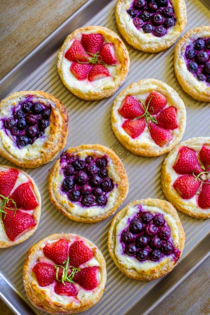 small desserts are arranged on a baking sheet with fresh berries and blueberries in the center