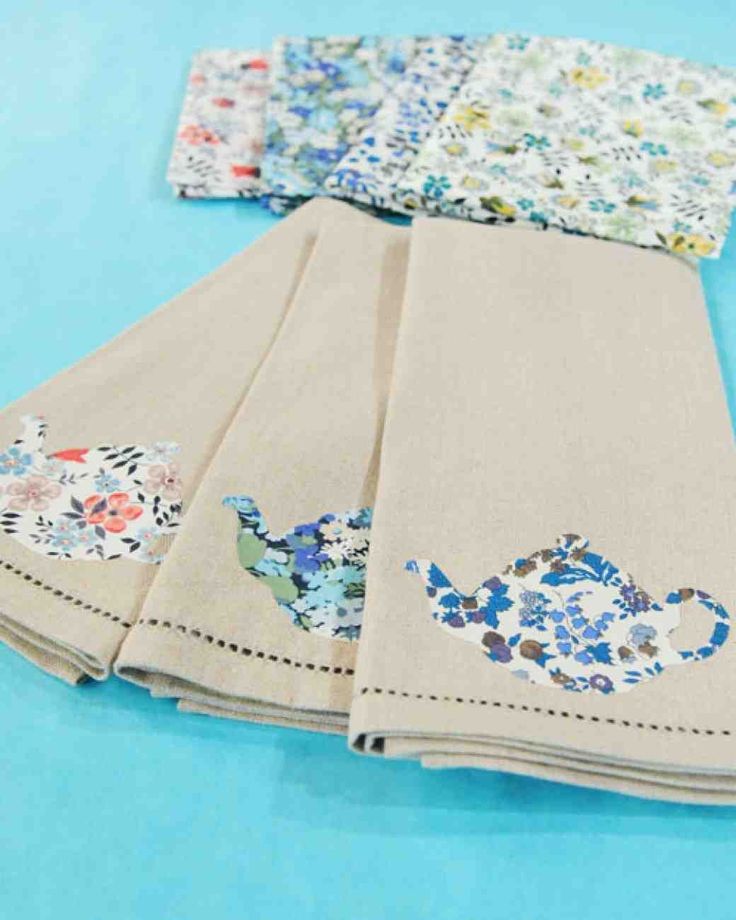 four napkins with floral designs on them sitting on a blue tablecloth covered surface