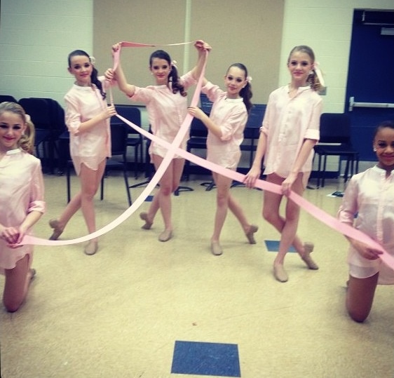 several girls in pink shirts and shorts holding ribbon