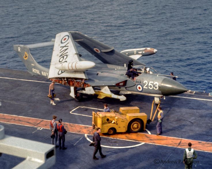 an air force jet sitting on top of a ship next to people standing near it