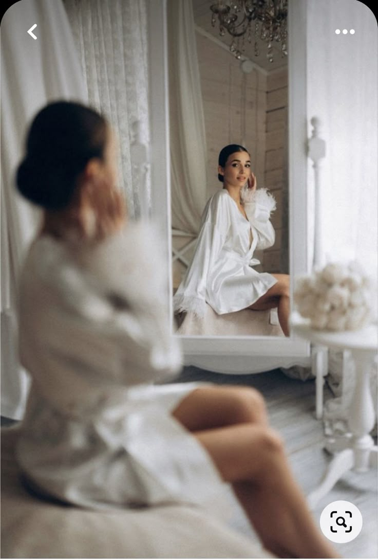 a woman sitting in front of a mirror with her legs crossed on the bed while looking at herself