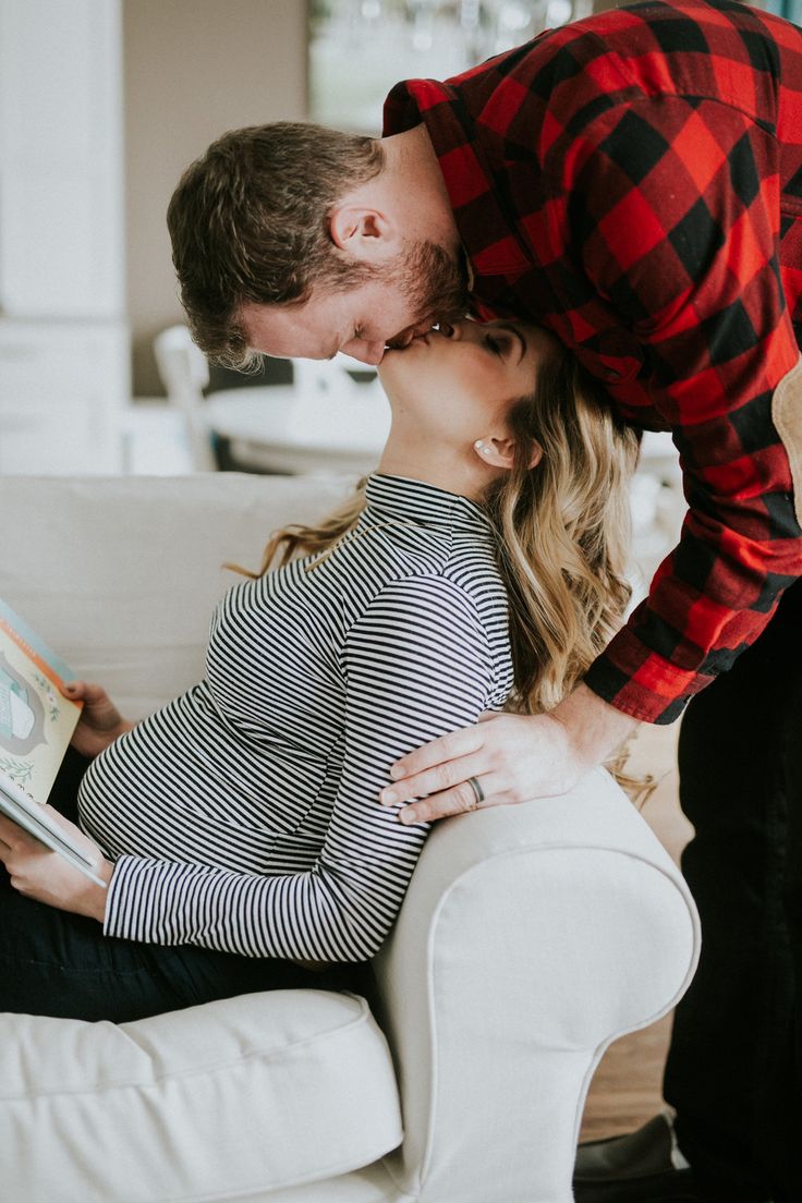 a man kissing a pregnant woman on the cheek while sitting on a white couch in a living room