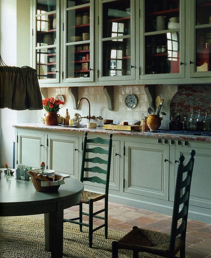 a dining room table and chairs in front of a kitchen with green cupboards on the wall