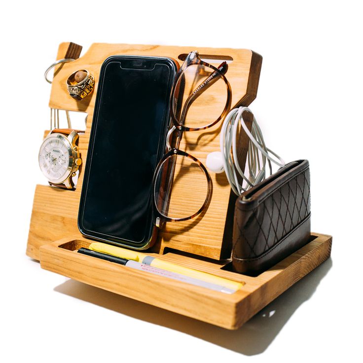 a cell phone and some glasses are on a wooden holder with pen, pencils, eyeglasses, and other items