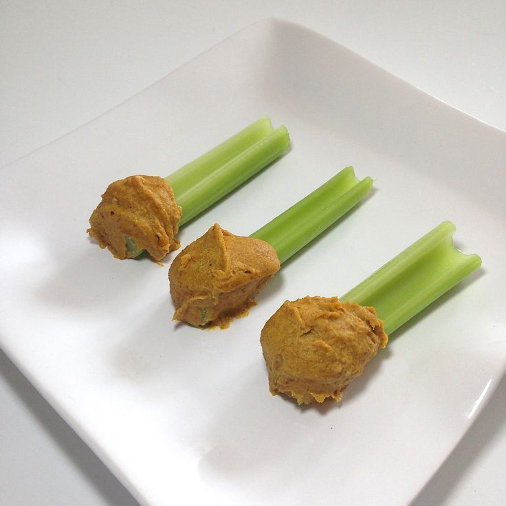 three celery sticks with peanut butter on them sitting on a square white plate