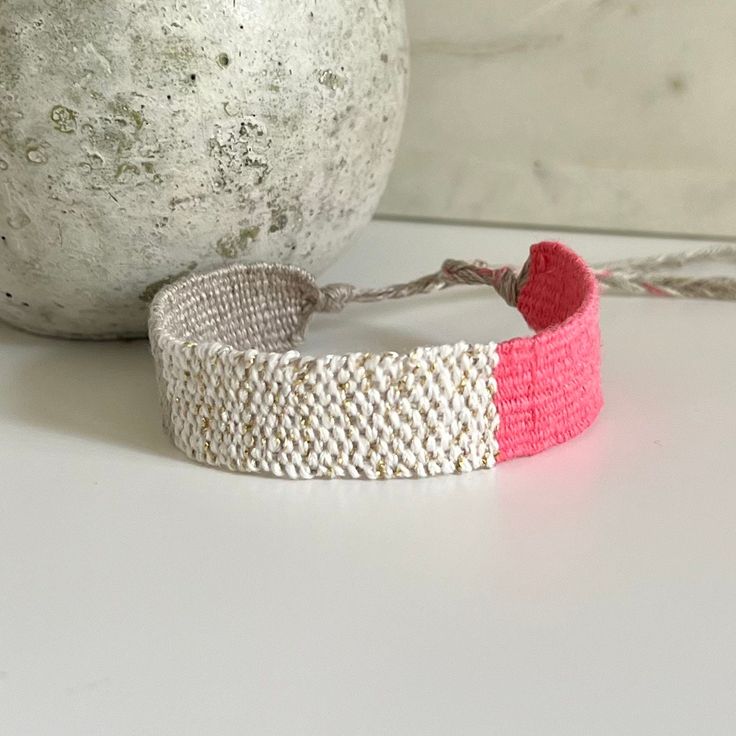 a pink and white bracelet sitting next to a gray vase on a table with a rope