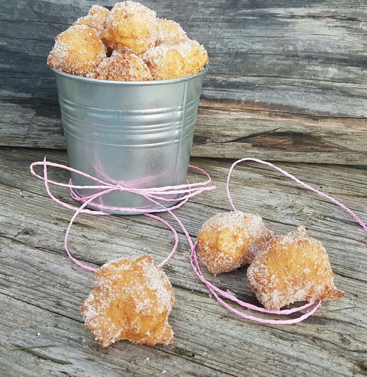 powdered sugar coated donuts are in a bucket on a wooden table next to string