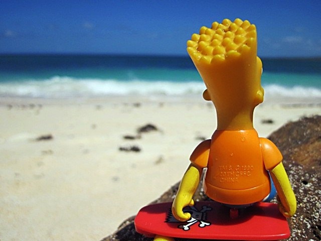 a toy figure sitting on top of a surfboard in front of the beach and ocean