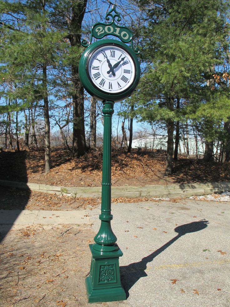 a green clock sitting on the side of a road