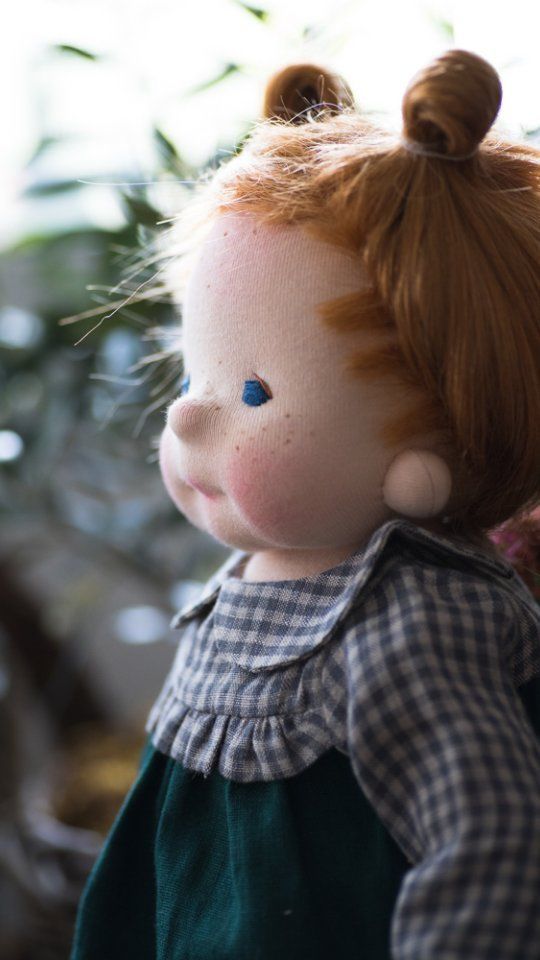 a doll with red hair and blue eyes wearing a green dress standing next to a tree