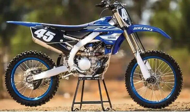 a blue and white dirt bike parked on top of a metal stand in the dirt