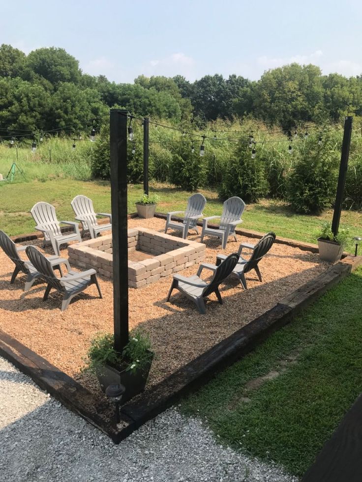 a fire pit surrounded by lawn chairs in the middle of a gravel area with grass