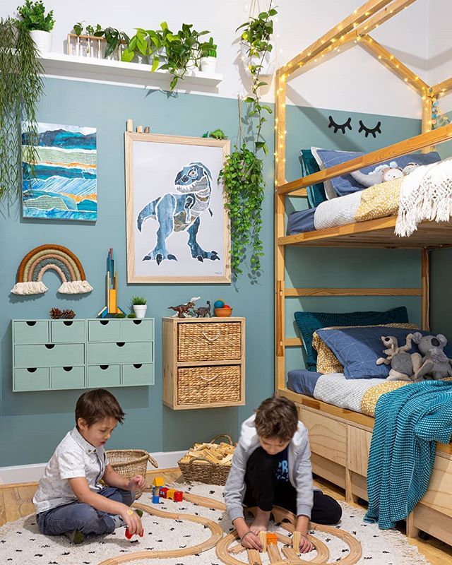 two children playing with wooden toys in a room decorated with blue walls and artwork on the walls